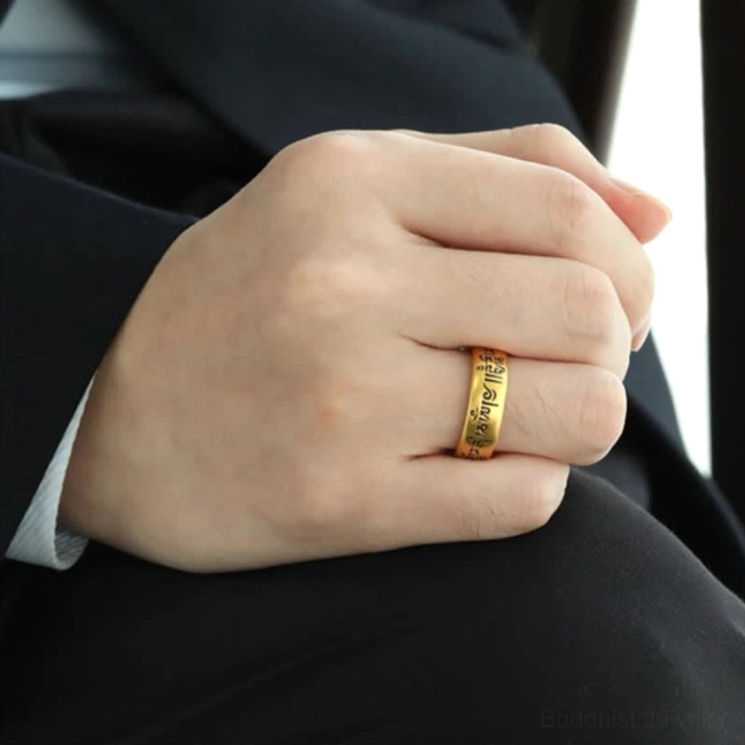 Man wearing Om Mani Padme Hum Buddhist ring on middle finger with business suit, golden finish visible in formal setting