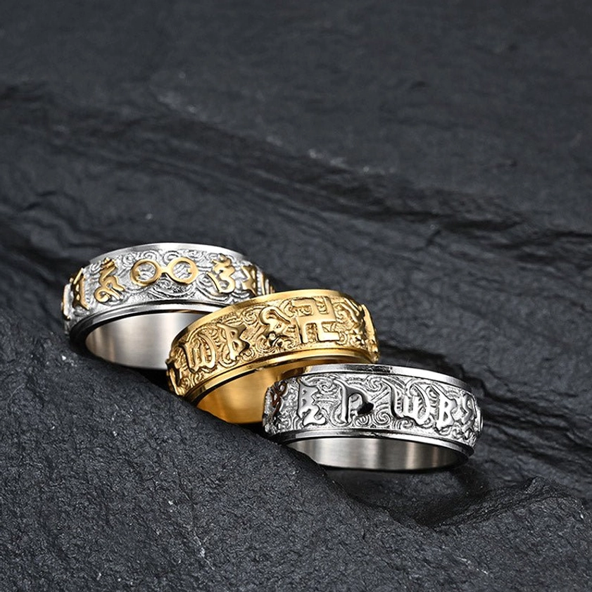 Collection of three Buddhist mantra titanium steel rings in silver and gold tones, stacked together showing distinct engraved Sanskrit patterns, overhead view