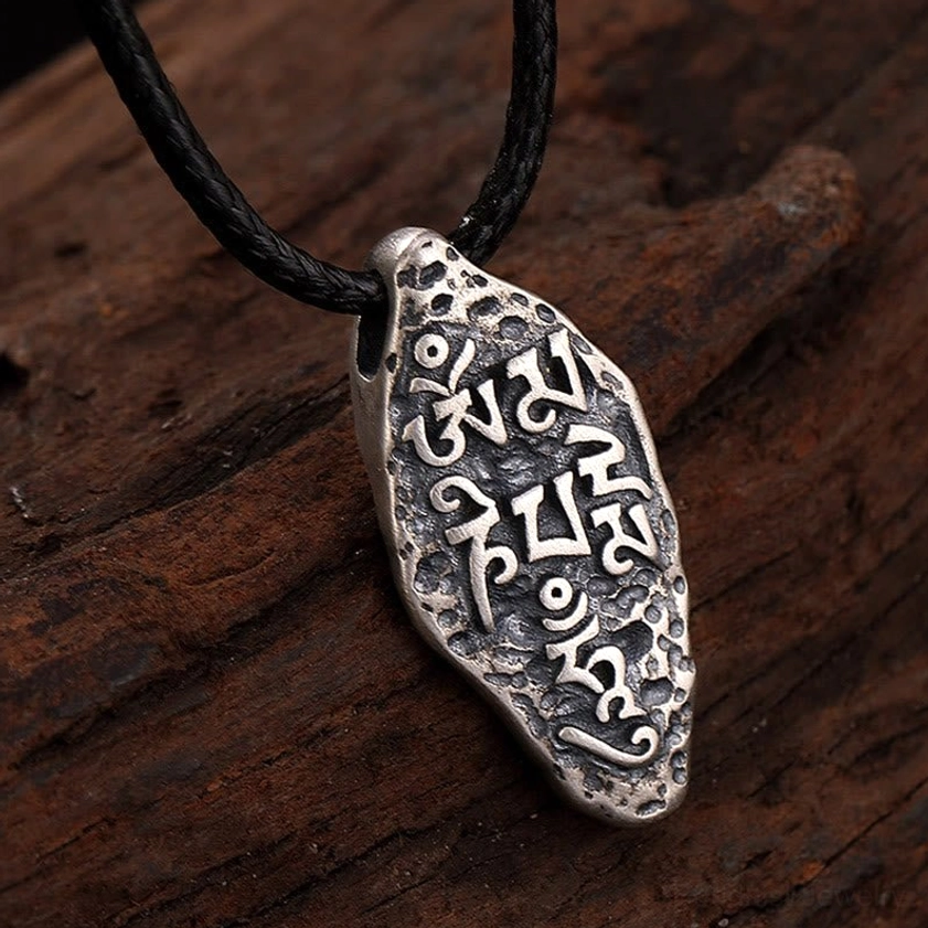 Vajra Om Mani Padme Hum pendant necklace front view on wooden background, clearly visible sacred mantra engravings with irregular drop shape