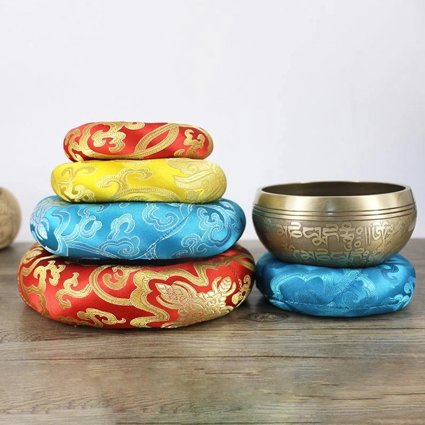 Tiered arrangement of handcrafted Buddhist singing bowl cushions on wooden surface, showcasing multicolor brocade embroidery details