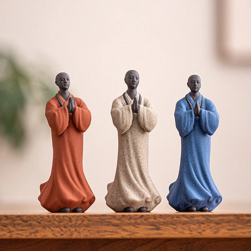Three Buddhist monk ceramic statues with detailed prayer beads displayed on wooden shelf in home meditation space