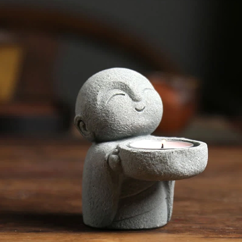 Smiling Buddhist monk tealight holder close-up - serene closed-eye expression on wooden surface
