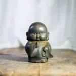 Handcrafted Buddhist monk meditation statue with dark grey rustic finish holding prayer beads, front view on wooden surface