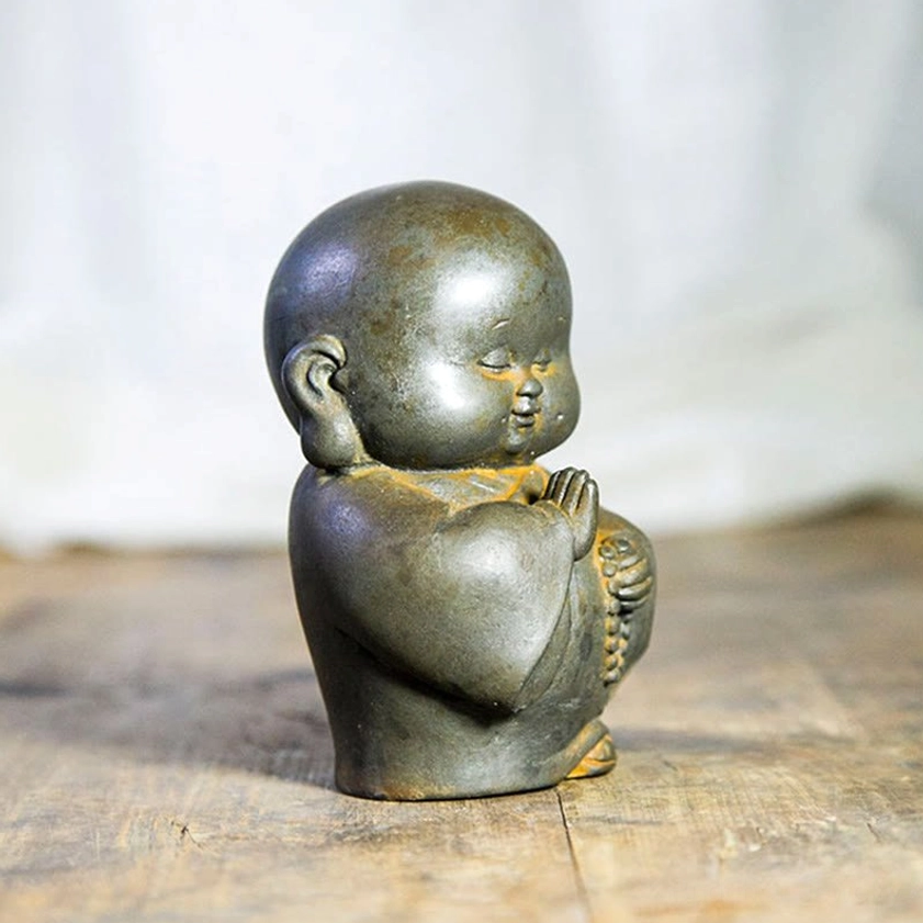 Handcrafted Buddhist monk ornament shown from left side profile, smooth matte dark tone with prayer hands pose
