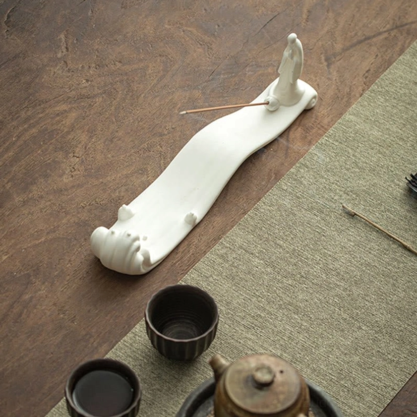 Handcrafted white ceramic Buddhist incense burner with tea cups and teapot on wooden tea table