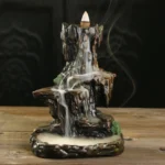 Handcrafted Buddhist mountain waterfall backflow incense burner with flowing smoke, dark brown resin with moss accents, front three-quarter view