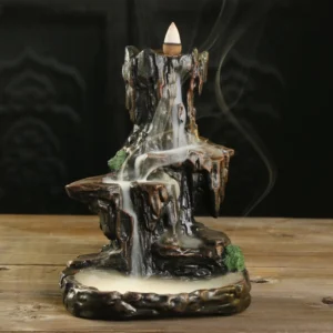 Handcrafted Buddhist mountain waterfall backflow incense burner with flowing smoke, dark brown resin with moss accents, front three-quarter view