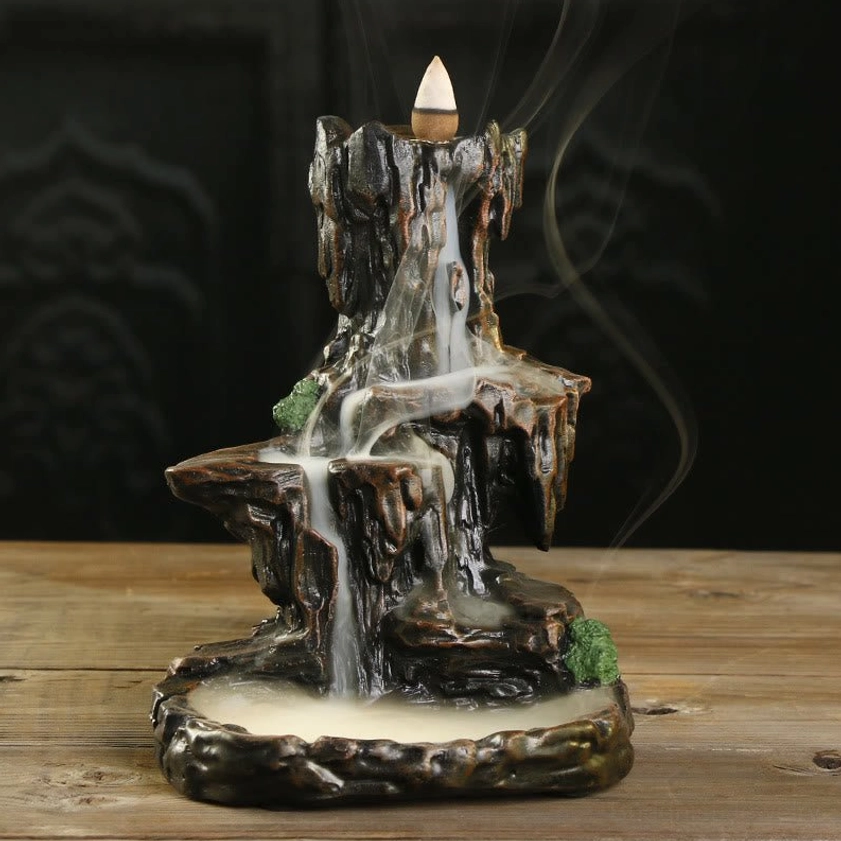 Handcrafted Buddhist mountain waterfall backflow incense burner with flowing smoke, dark brown resin with moss accents, front three-quarter view