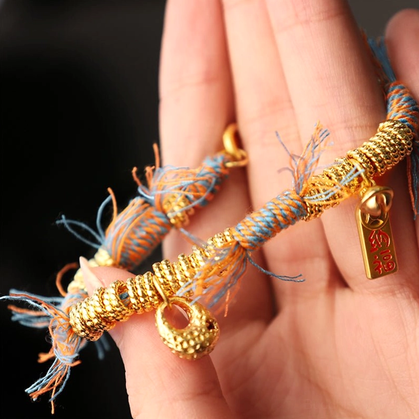 Handmade Buddhist string bracelet held in palm showing hanging charm, tassel fringe details, and authentic braided rope texture for spiritual protection