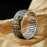 Chinese Zodiac Natal Buddha adjustable copper ring with vintage silver finish and gold-plated Buddha statue, shown on dry leaf with engraved sutras and cloud patterns
