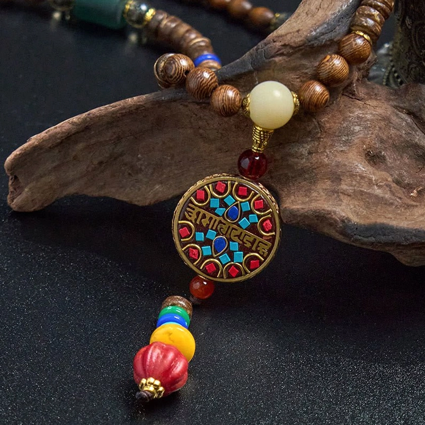 Wooden beaded Buddhist necklace with copper accent bead and multi-color tassel on driftwood background