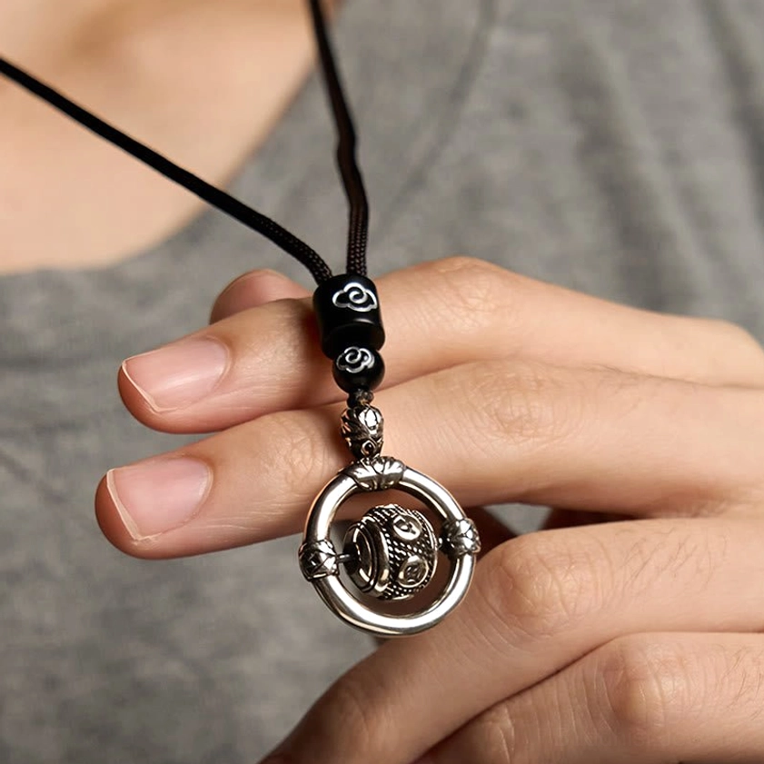 Buddhist copper pendant necklace being held, displaying black cord with silver rotating bead and cloud-patterned cord stops