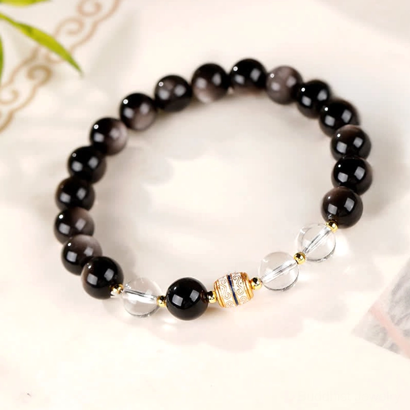 Silver Sheen Obsidian Buddhist bracelet with sacred Dzi bead focal point, displayed on light background with leaf decoration