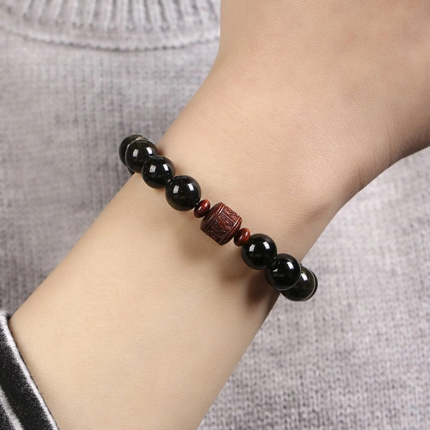 Multiple variations of rainbow and gold sheen obsidian bracelets with different engraved symbols displayed together