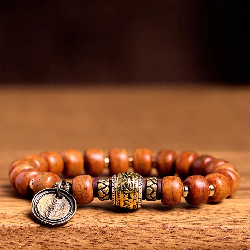 Buddhist camel bone protection bracelet flat lay on wooden surface, displaying reddish-brown bone barrel beads with engraved metal OM charm