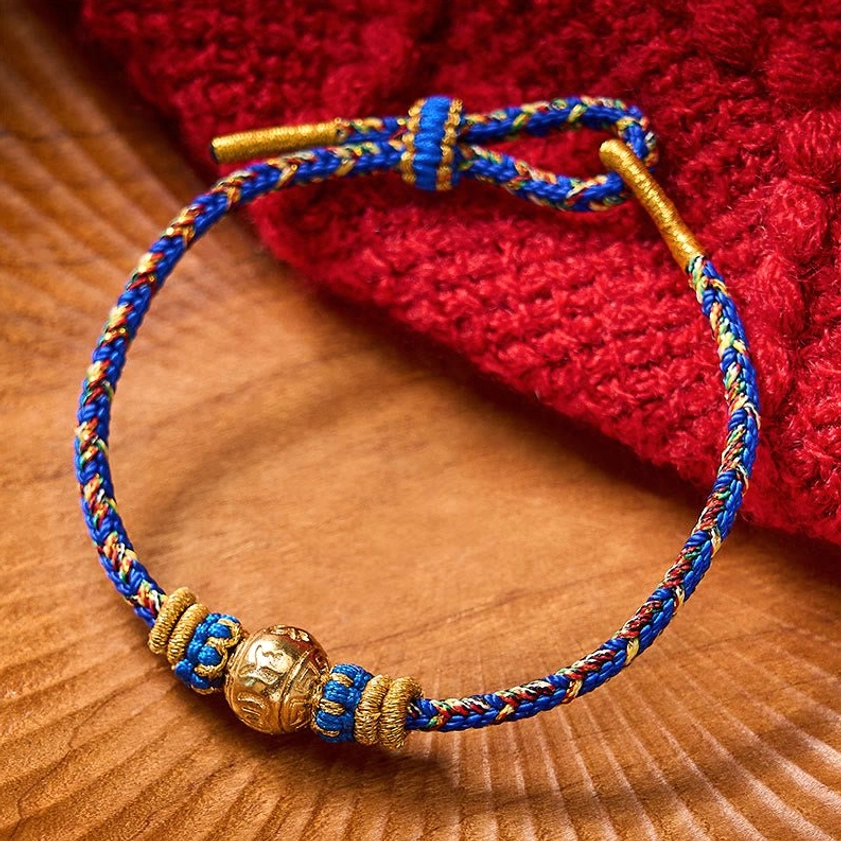 Handmade Buddhist string bracelet with tri-color woven cord and central mantra bead on wooden background