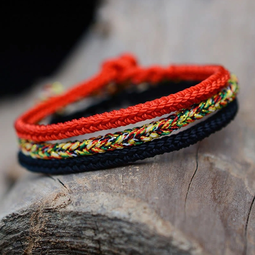 Close-up overhead view of handcrafted eight-strand Buddhist braided bracelet showing red outer band, colorful center layer, and black base on textured wood