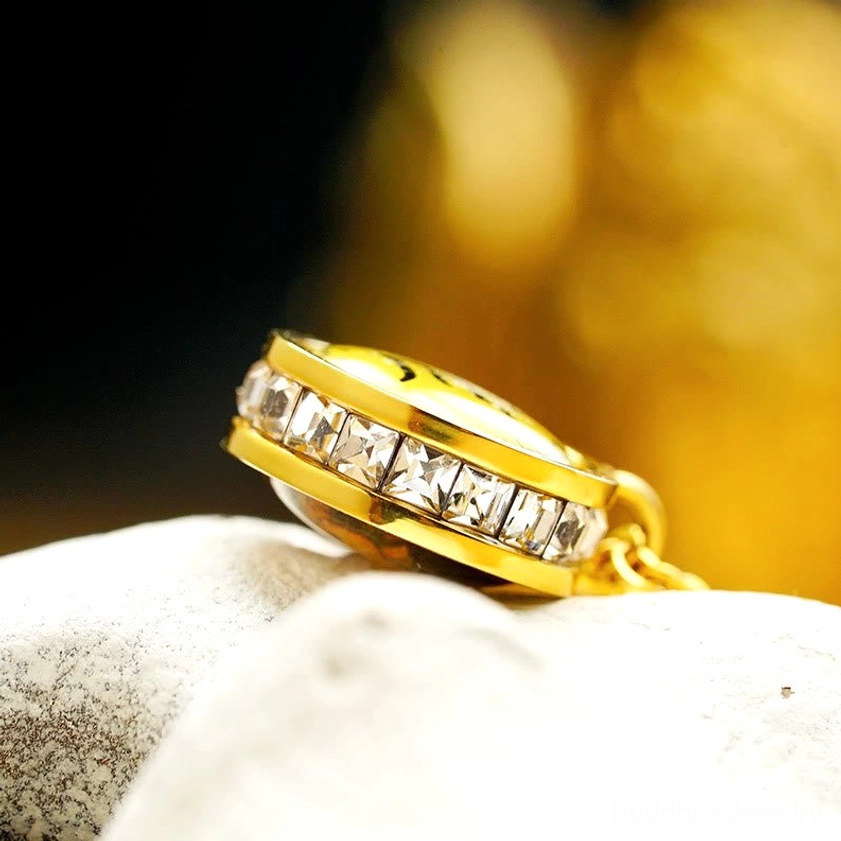 Buddhist deity pendant with crystal-studded border - polished titanium steel on stone display