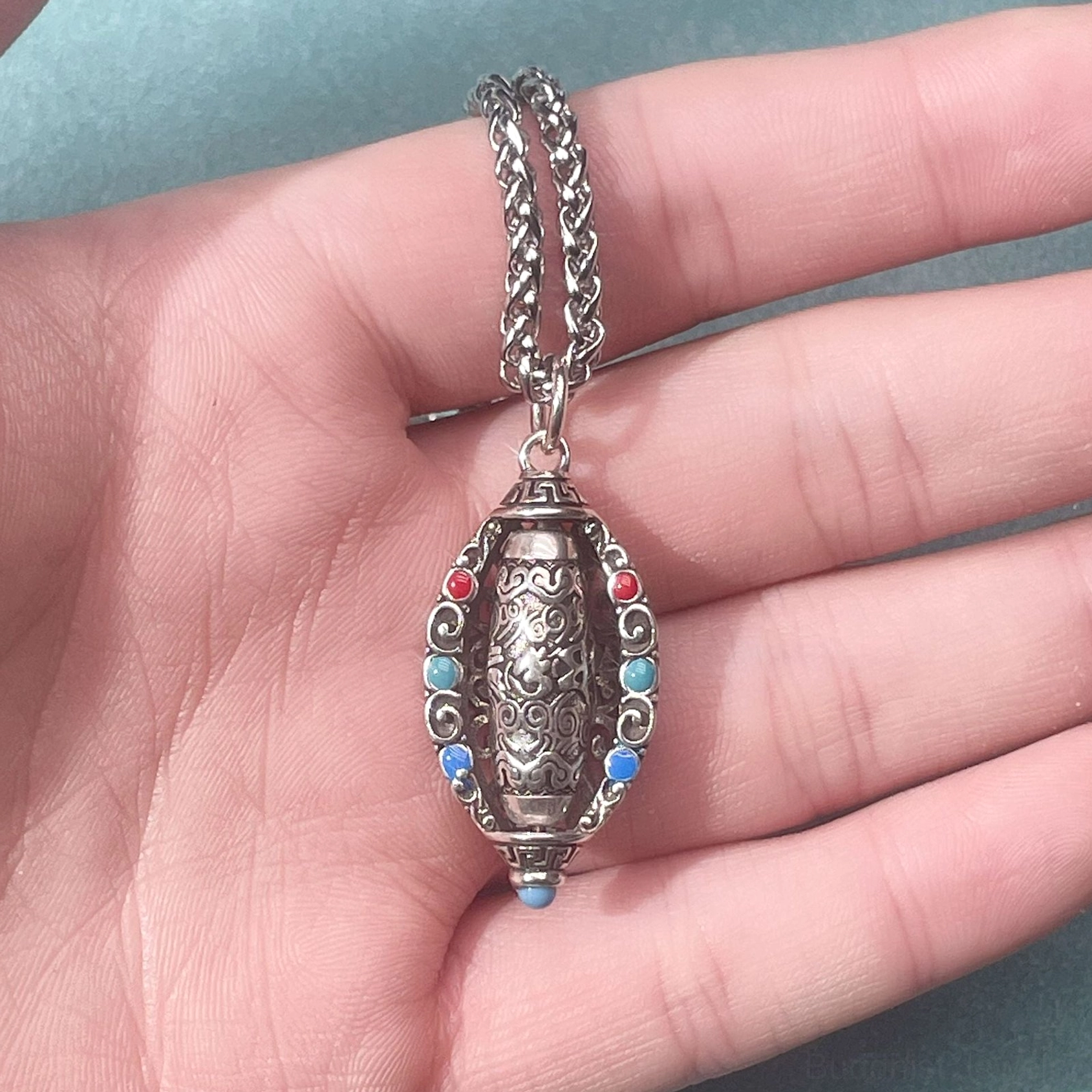 Buddhist mantra pendant in hand showing carved sacred symbols and colored gemstone inlay details with compact size perspective