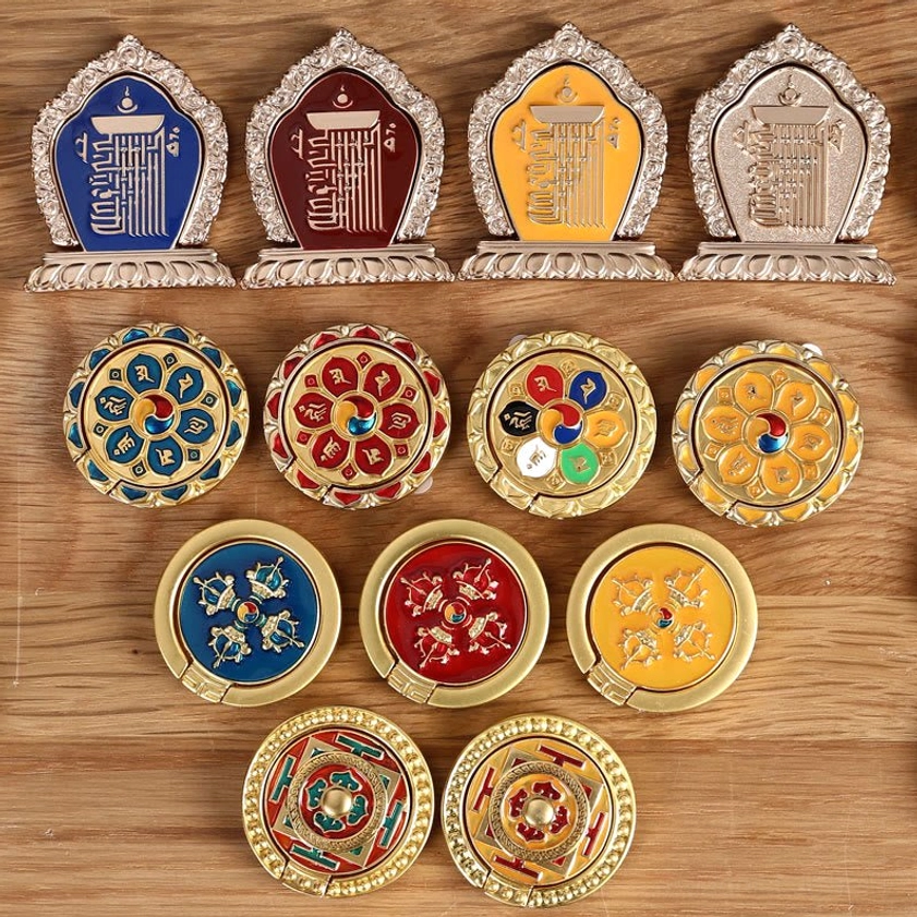 Assorted Buddhist mantra phone ring holders in multiple colors and patterns including six-character mantra and mandala designs on wooden surface