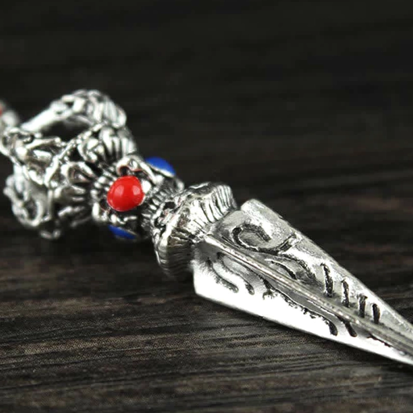 Close-up side view of traditional phurba dagger charm with silver metal and red blue enamel accents