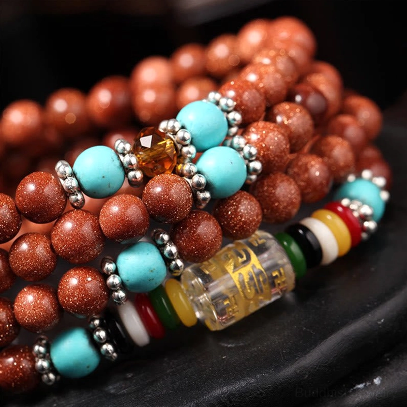 Goldstone mala bracelet side view with silver spacers, multi-color dividers, and six-word mantra bead on wooden base
