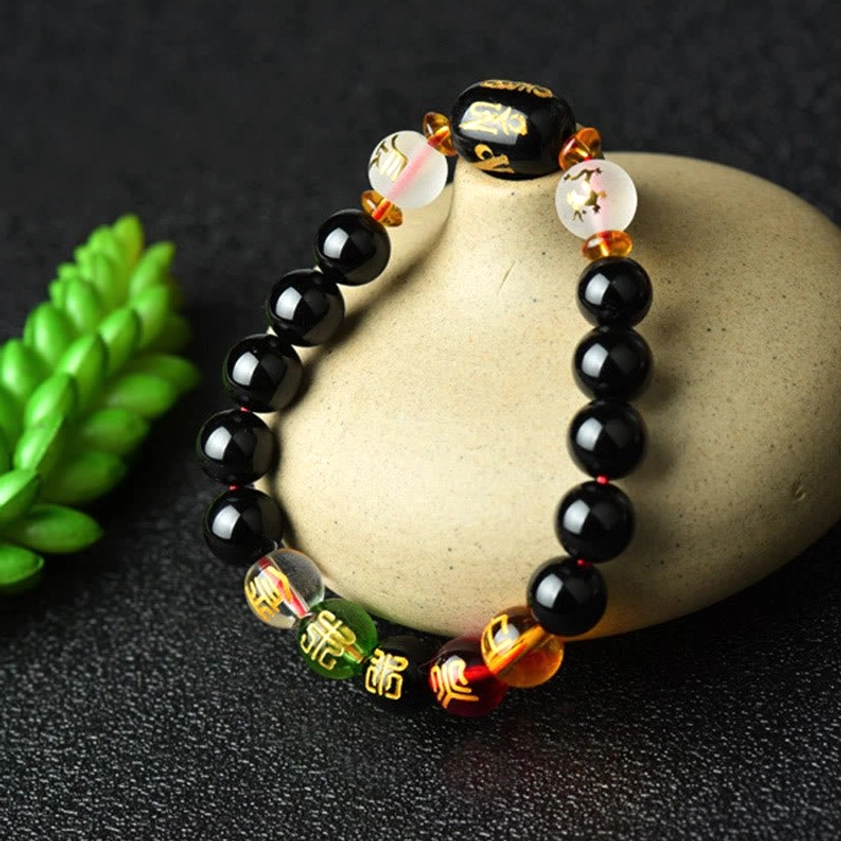Handmade Buddhist bracelet with polished black onyx, green and red accent beads, engraved prayer bead on wooden tray with plants
