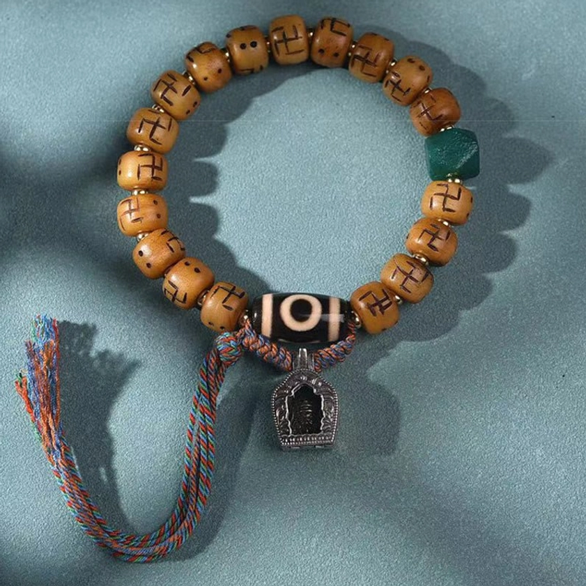 Tibetan Buddhist prayer bracelet featuring tan bone beads, green accent stone, metal shrine pendant, and colorful woven tassel