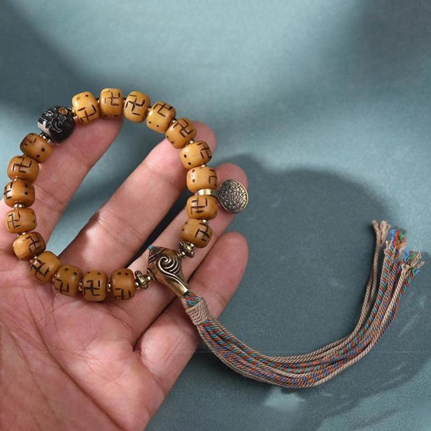 Buddhist prayer bracelet with tan camel bone beads, metal charm disc, and spiritual tassel displayed in palm