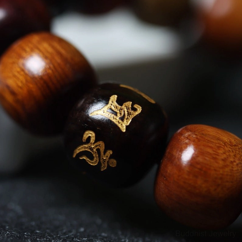 Macro close-up detail of smooth barrel-shaped wooden beads with black bead featuring embossed golden Sanskrit Om Mani Padme Hum mantra