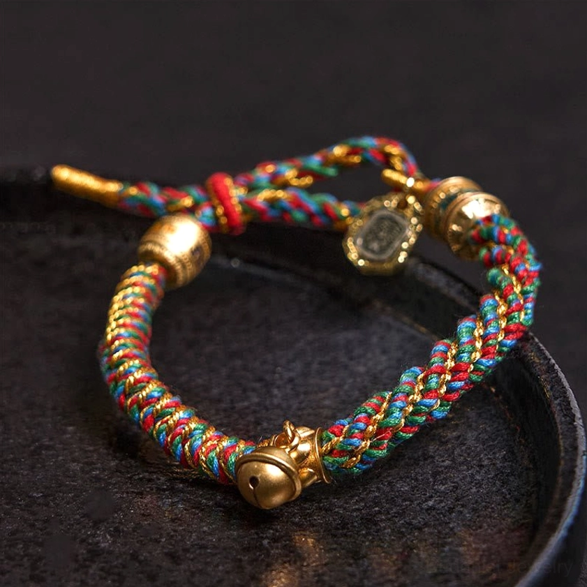 Close-up side view of Buddhist prayer bracelet with rainbow braided cord, gold beads, and protective amulet pendants