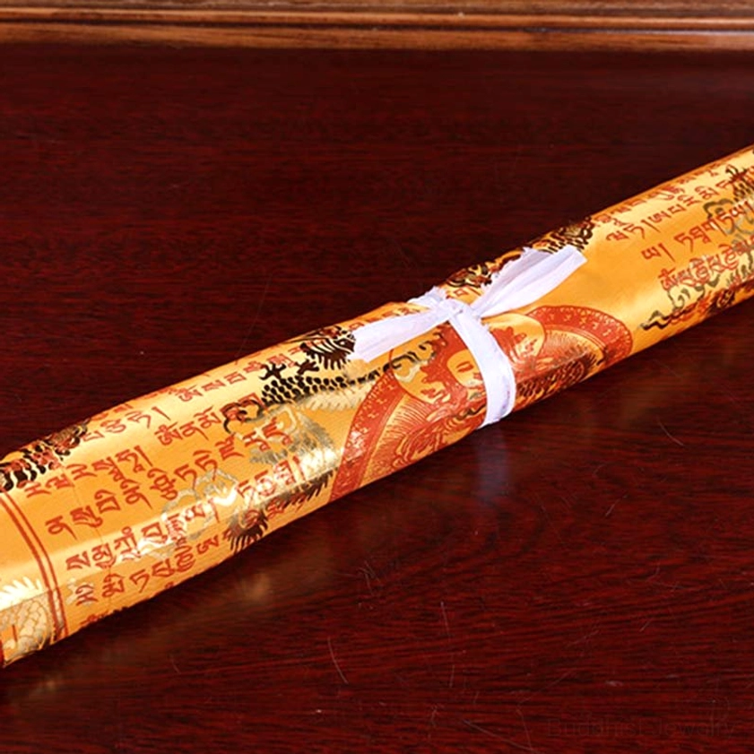Single rolled buddhist prayer flag with golden-red fabric printed with tibetan sutras secured with white strap on wooden table