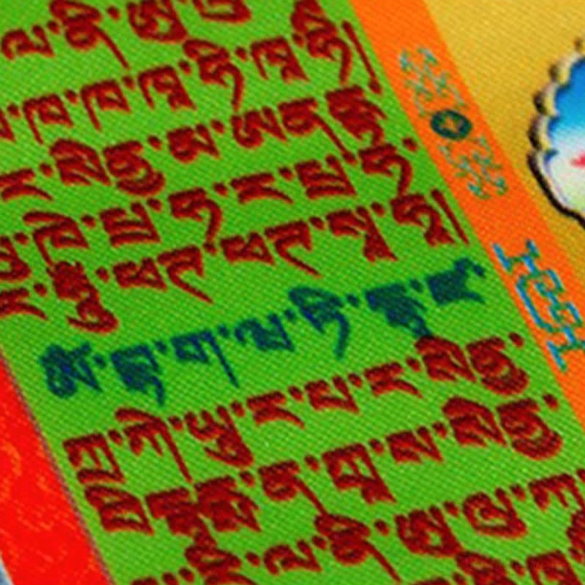 Prayer flag textile macro close-up green base multicolor Buddhist script woven fabric texture detail