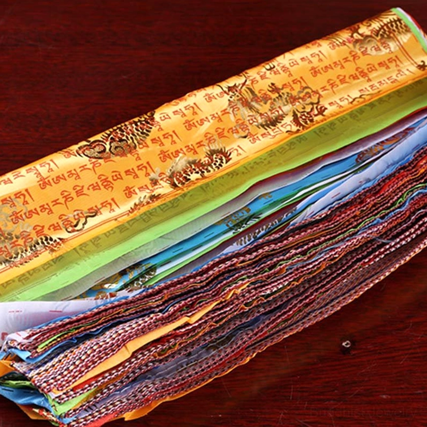 Stacked five color buddhist prayer flags showing woven edges and tibetan sutras on dark wooden surface, loose layout