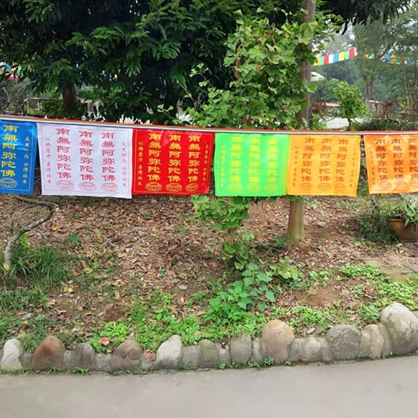 Multi-color Buddhist prayer flags neatly arranged in shaded garden area, showing eye-level view of strung sacred sutras and spiritual banners