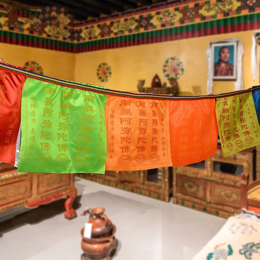 Colorful Buddhist prayer flags displayed indoors in Tibetan-style space, featuring printed sutras and sacred symbols across 5-color prayer flag banners