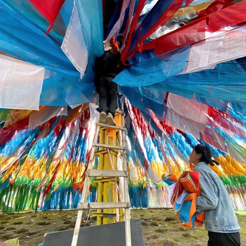 Workers installing Buddhist prayer flags at high-altitude mountain location