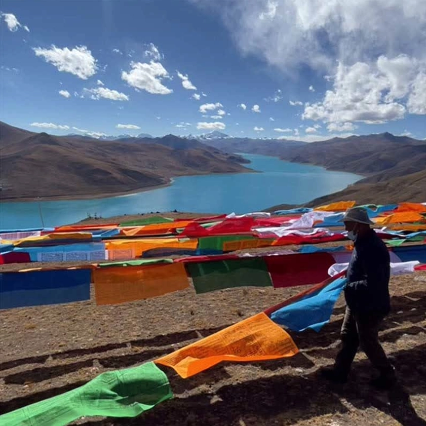 Man adjusting Buddhist prayer flags at lakeside mountain landscape installation