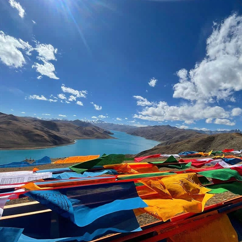 Buddhist prayer flags display at sunny highland lakeside with blue sky and clouds