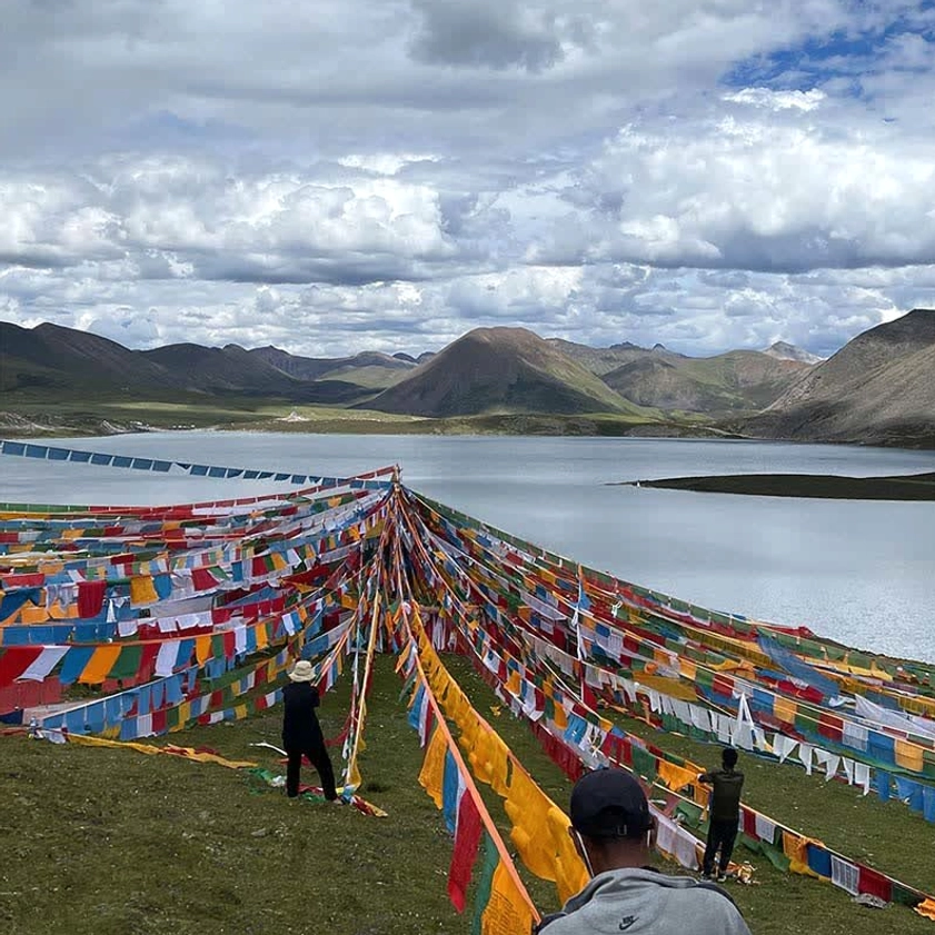 Outdoor Buddhist prayer flags installation at highland lakeside with mountains and grassland