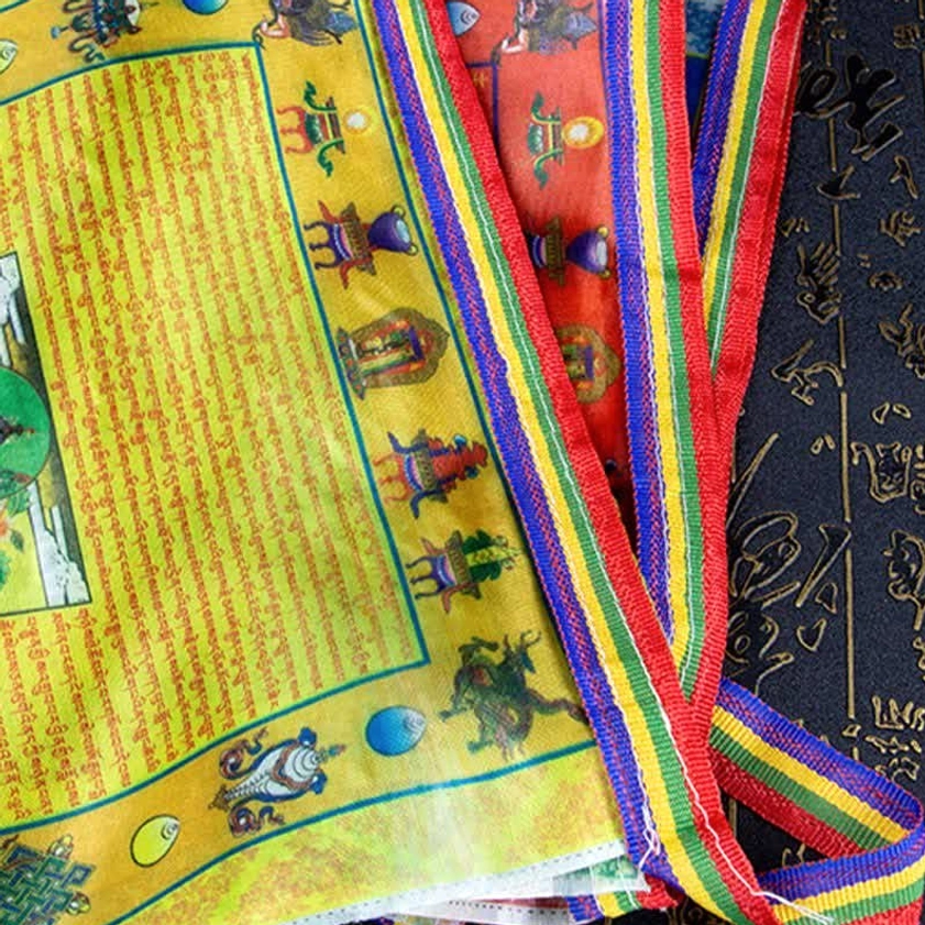 Angled view of stacked Buddhist prayer flags with multicolor woven edge straps and printed religious iconography