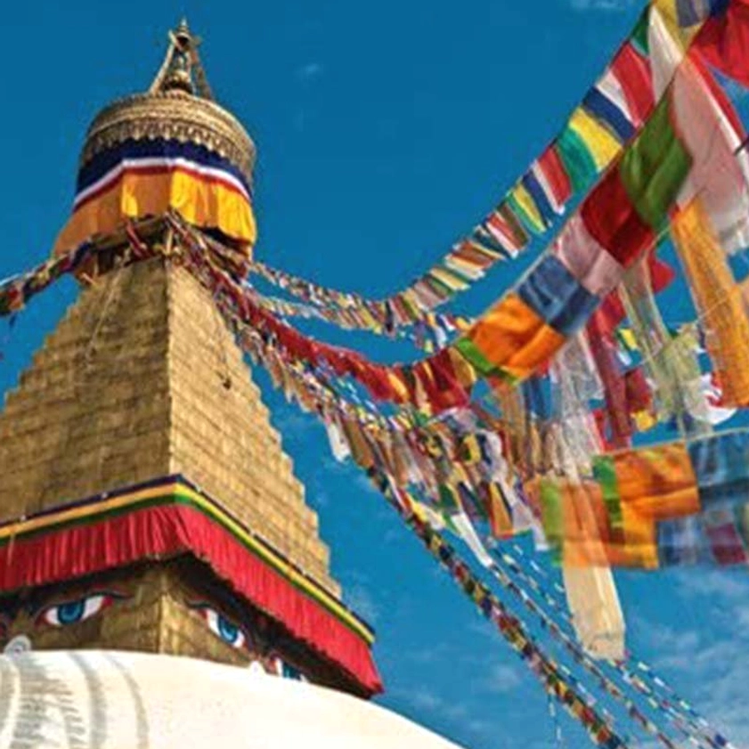 Fluttering Buddhist prayer flags in front of golden stupa with blue sky, showing traditional outdoor spiritual setup