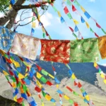 5-color Buddhist prayer flags with windhorse and dragon patterns hanging outdoors with mountains and blue sky background