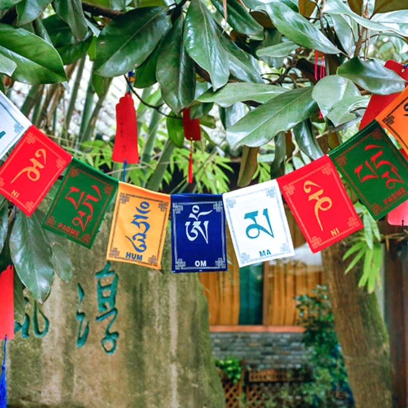 Buddhist prayer flags with Windhorse and Om Mani Padme Hum mantra hanging in garden with green foliage backdrop