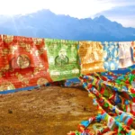 Buddhist prayer flags with windhorse lung ta design displayed outdoors in mountain wilderness setting, showing all five sacred colors blue white red green yellow