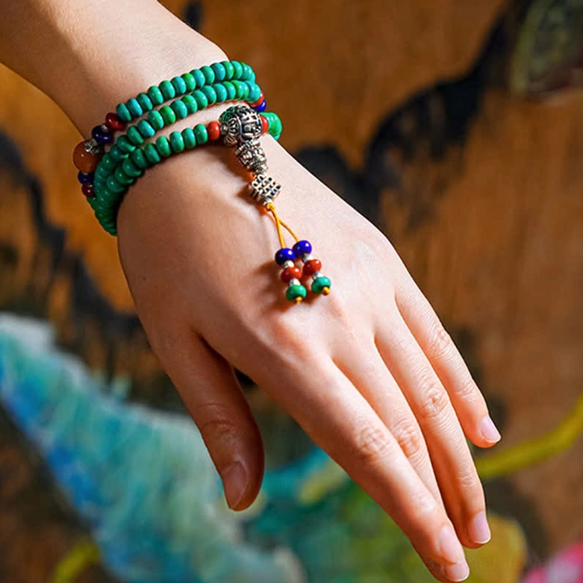 Wearing turquoise Buddhist mala bracelet on wrist with hand-painted dzi bead and tassel pendant