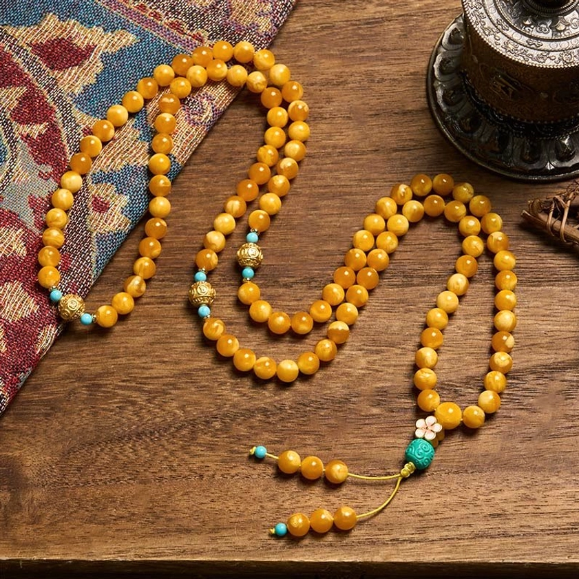 Coiled amber Buddhist mala necklace with turquoise and gold accent beads, side angle view on wooden table with ethnic textile