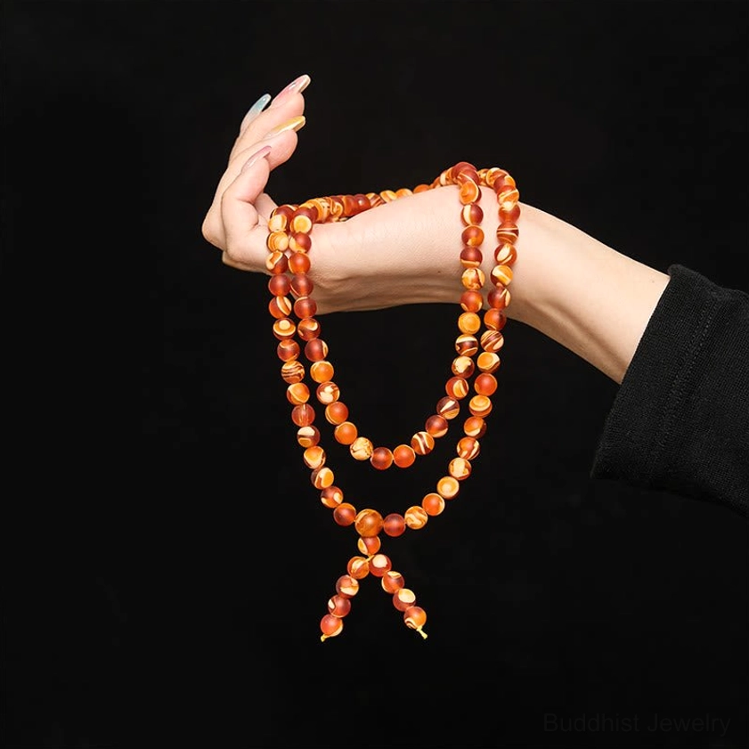 Hand-held multi-layer amber mala necklace worn on woman's hand with orange-red beads