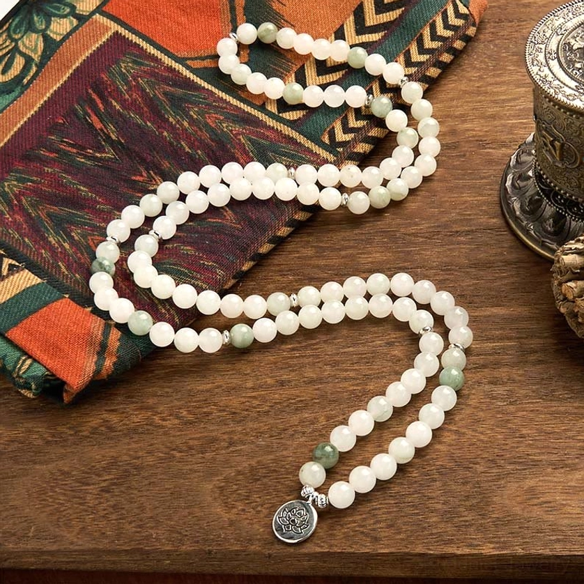 Natural jade prayer mala beads strung loosely on fabric, featuring silver lotus charm and white jade stones