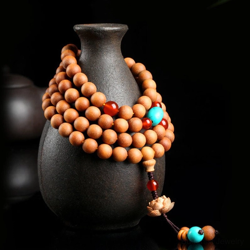Side view of handcrafted sandalwood Buddhist mala wrapped around dark ceramic vase, showing detailed bead texture and lotus tassel pendant